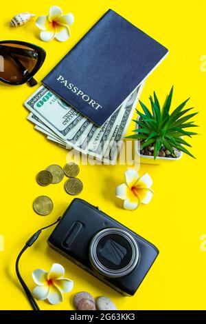 Reisekonzept für den Sommer. Reisepass, Geld, Sonnenbrille und eine Kamera auf gelbem Hintergrund. Vertikales Format, für Text platzieren. Stockfoto