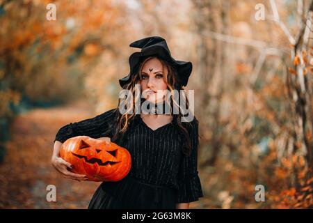 Mädchen gekleidet als Hexe hält Kürbis auf dem Hintergrund eines Herbstwaldes. Stockfoto