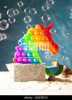 Pop it Spielzeug, Regenbogenfarben, in Form eines Einhorns auf dem Podium auf einem hellen Hintergrund. Mehrfarbige, sensorische Anti-Stress-Spielzeug Fidget Pop it und so Stockfoto