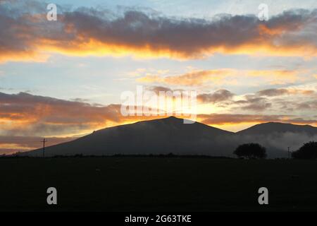 Schöner goldoranger Sonnenuntergang und Wolken über einem Berg in der Landschaft in Pwllheli, Nordwales Stockfoto