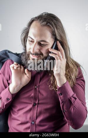 Porträt eines jungen Geschäftsmannes aus dem Nahen Osten mit Bart und langen Haaren, während er ein Gespräch auf dem Mobiltelefon führt Stockfoto