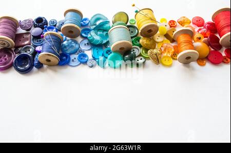 Viele Knöpfe und Rollen mit bunten Fäden, auf weißem Hintergrund in den Farben des Regenbogens ausgelegt. Speicherplatz kopieren. Stockfoto