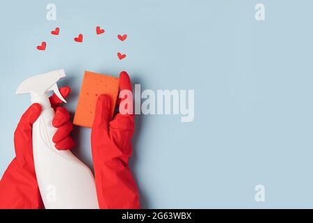 Eine Hand in roten Handschuhen hält einen Spray mit Reinigungsflüssigkeit und Schwamm auf einem blauen Hintergrund mit Herzen. Speicherplatz kopieren Stockfoto