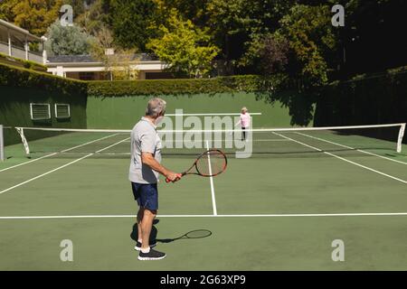 Ältere kaukasische Paare spielen gemeinsam Tennis auf dem Platz Stockfoto
