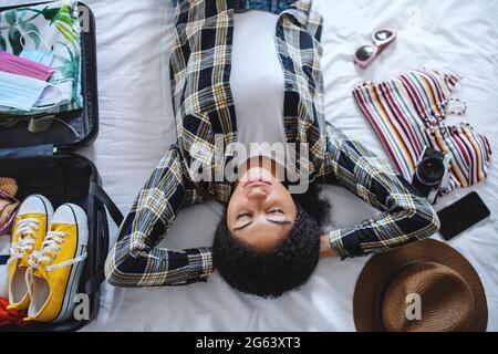 Draufsicht auf junge Frau mit Kofferpackung für den Urlaub zu Hause, Coronavirus-Konzept. Stockfoto