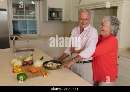Ein älteres kaukasisches Paar kocht zusammen und lächelt in der Küche Stockfoto