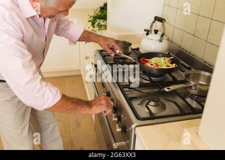 Leitender kaukasischer Mann kocht und hält eine Bratpfanne in der Küche Stockfoto