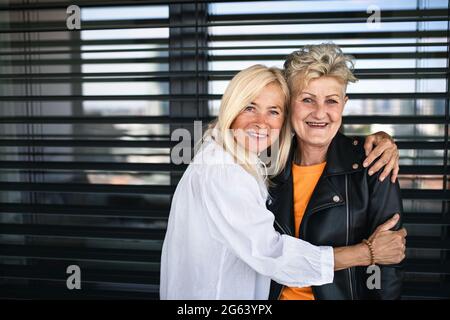 Zwei ältere Freundinnen, die draußen vor dem Fenster stehen und die Kamera betrachten. Stockfoto