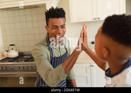 Glücklicher afroamerikanischer Vater und Sohn hoch fiving in der Küche vor dem Kochen Stockfoto