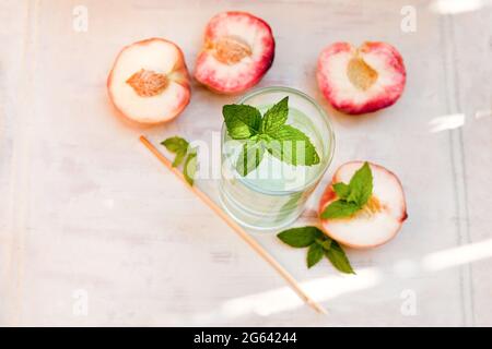 Erfrischender Eistee mit Pfefferminze und Pfirsichen auf grauem Hintergrund, selektiver Fokus. Wassergetränk mit Pfirsichen Stockfoto
