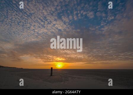 Sonnenuntergang mit leuchtend orangefarbenen Farben vor einem Himmel mit weißen Wolken vom Strand einer Watteninsel im Norden der Niederlande aus gesehen Stockfoto