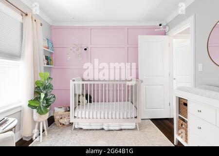 Ein gemütliches Kinderzimmer mit einem Kinderbett vor einem hellrosa Brett und einer Wand mit Akzenten aus Batten. Ein Handy hängt über dem Kinderbett und Kameras sind an der Wand montiert. Stockfoto