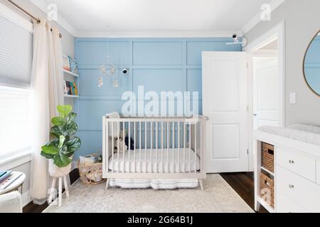 Ein gemütliches Kinderzimmer mit einem Kinderbett vor einem hellblauen Brett und einer Wand mit Akzenten aus Batten. Ein Handy hängt über dem Kinderbett und Kameras sind an der Wand montiert. Stockfoto
