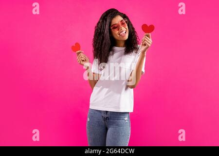 Portrait von ziemlich trendy fröhliche Mädchen in den Händen halten kleine Herzkarten isoliert über lebendige rosa fuchsia Farbe Hintergrund Stockfoto