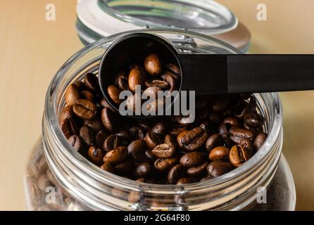 Kaffeebohnen in einer transparenten Schüssel mit einem Messlöffel aus Kunststoff Stockfoto