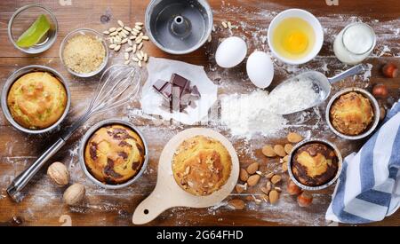 Hausgemachte Muffins und Backkuchen mit Kochwerkzeugen und Zutaten auf holzbemehltem Hintergrund, Draufsicht, flach liegend. Stockfoto