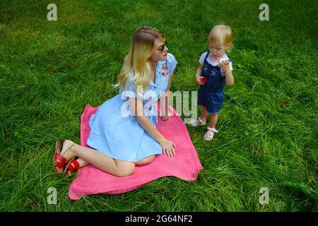 Eine junge Mutter und ihre kleine Tochter blasen Seifenblasen auf das grüne Gras im Stadtpark. Erholung im Freien. Kindheit, Familie Stockfoto