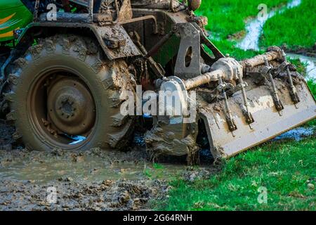 Feld „Traktorpflüge“. Nahaufnahme von schweren Maschinen, die am hinteren Ende des Traktors befestigt sind und mit Schlamm bedeckt sind, die durch das schlammige Feld pflügen. Stockfoto