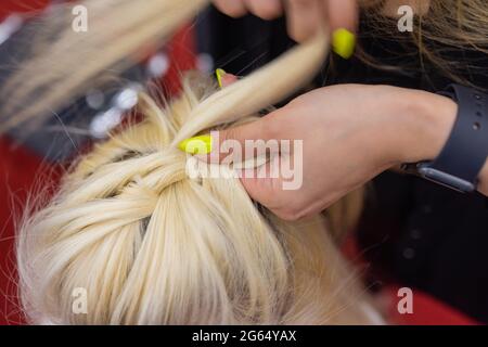 Die Hände der Frauen weben ein Zopf auf den Kopf der Brünette Stockfoto