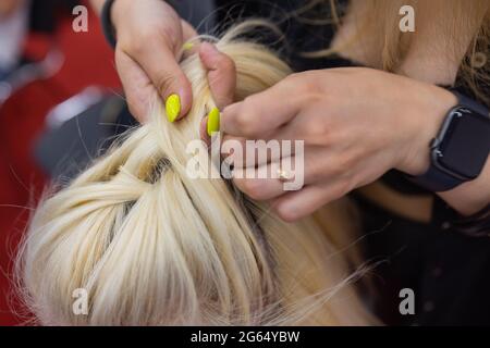 Die Hände der Frauen weben ein Zopf auf den Kopf der Brünette Stockfoto