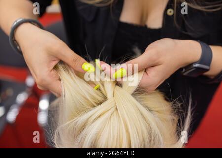 Die Hände der Frauen weben ein Zopf auf den Kopf der Brünette Stockfoto