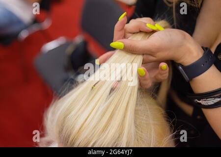 Die Hände der Frauen weben ein Zopf auf den Kopf der Brünette Stockfoto