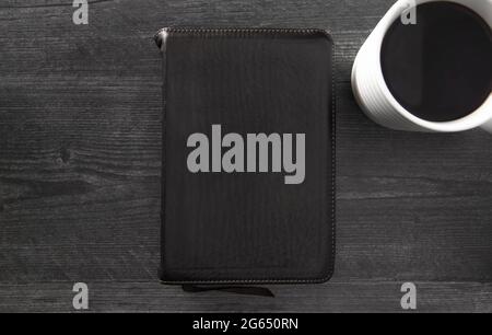Eine einzelne schwarze Bibel auf einem schwarzen Holztisch Stockfoto