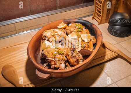 Hausgemachtes gegrilltes Hähnchen mit in Stücke geschnittenen Gewürzen in roter Keramik-Backform auf Holzbrett. Stockfoto