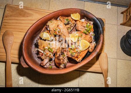 Hausgemachtes gegrilltes Hähnchen mit in Stücke geschnittenen Gewürzen in roter Keramik-Backform auf Holzbrett. Stockfoto