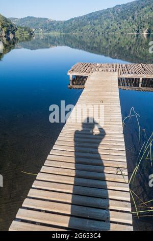 Hölzerner Pier und die Silhouette des Fotografen am See Lago Tilquilco im Nationalpark Huerquehue, Chile Stockfoto