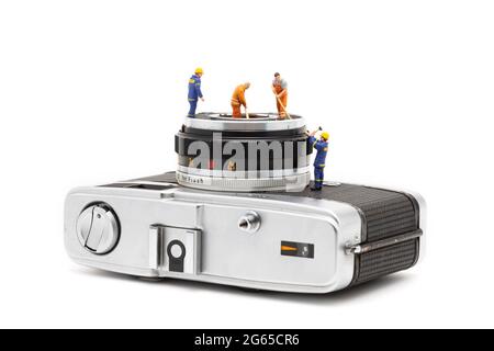 Miniaturmenschen reinigen alte Kameraobjektive auf weißem Hintergrund. Stockfoto