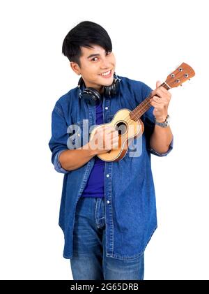 Junger asiatischer Mann mit Kopfhörern, der eine Ukulele-Gitarre spielt. Porträt auf weißem Hintergrund mit Studiolicht. Nahaufnahme Stockfoto