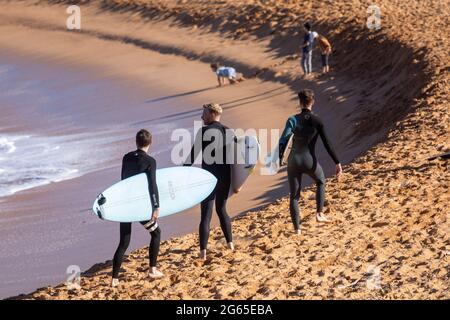 Australische Surfer tragen ihre Surfbretter am Avalon Beach in Sydney an einem sonnigen Wintertag, NSW, Australien Stockfoto