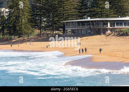 Australische Surfer tragen ihre Surfbretter am Avalon Beach in Sydney an einem sonnigen Wintertag, NSW, Australien Stockfoto