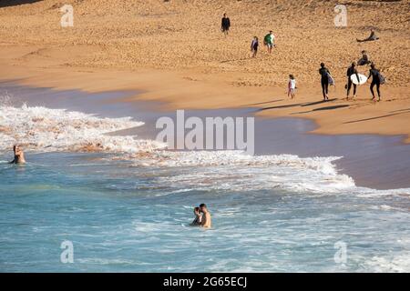 Australische Surfer tragen ihre Surfbretter am Avalon Beach in Sydney an einem sonnigen Wintertag, NSW, Australien Stockfoto