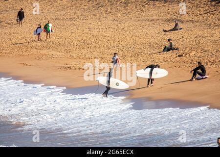 Australische Surfer tragen ihre Surfbretter am Avalon Beach in Sydney an einem sonnigen Wintertag, NSW, Australien Stockfoto