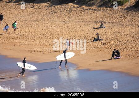 Australische Surfer tragen ihre Surfbretter am Avalon Beach in Sydney an einem sonnigen Wintertag, NSW, Australien Stockfoto