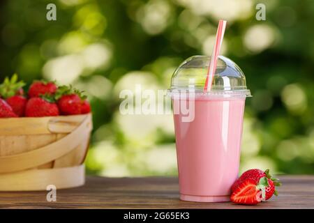 Erdbeer-Smoothie in Einweg-Plastikglas auf Holztisch Stockfoto