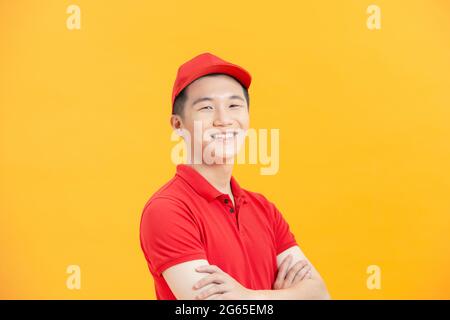 Selbstbewusster asiatischer Lieferer lächelt und blickt mit gekreuzten Armen auf die Kamera. Stockfoto