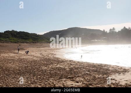 Am frühen Morgen geht die Sonne am Avalon Beach in Sydney unter, während Surfer zu den Wellen des Ozeans, NSW, Australien, fahren Stockfoto