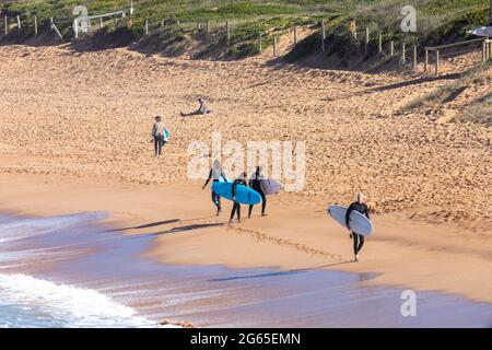 Australische Surfer tragen ihre Surfbretter am Avalon Beach in Sydney an einem sonnigen Wintertag, NSW, Australien Stockfoto