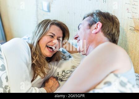 Ein Paar mittleren Alters lachte auf dem Bett. Stockfoto