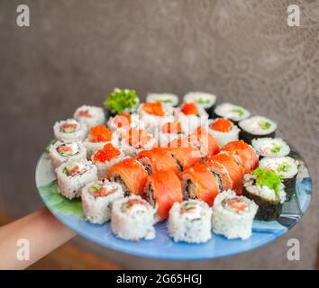 Sushi und Brötchen zu Hause zubereiten. Sushi mit Meeresfrüchten, Salat und weißem Reis. Essen für Familie und Freunde. Eine Reihe verschiedener Brötchen und Sushi auf einem Tablett Stockfoto