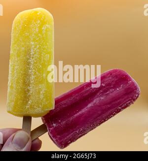 Hand mit gelbem und violettem Popsicle auf gelbem Hintergrund Stockfoto