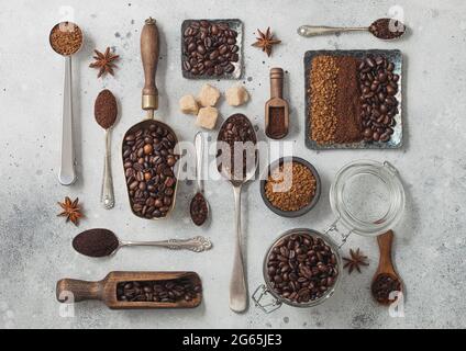Gefriergetrocknetes Instant-Kaffee-Granulat mit gemahlenem Kaffee und Bohnen in verschiedenen Löffeln und Messlöffeln auf schwarzem Hintergrund mit Glasglas und Stahlplatten. Bis Stockfoto