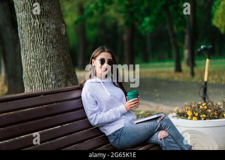 Junge Frau, die im Park auf einer Bank sitzt, auf einem Roller reitet Stockfoto