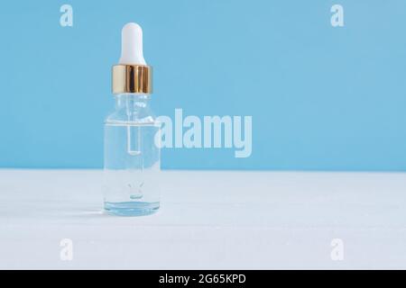 Bernsteinglas Serumflasche auf blauem Hintergrund. Trendiges Beauty-Produkt für junge Haut. Zusätzlicher feuchtigkeitsspendender Schritt im täglichen Gesichtsalltag Stockfoto