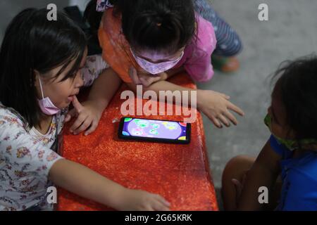 Drei thailändische Kinder spielen zusammen ein Logikspiel auf einem Smartphone Stockfoto