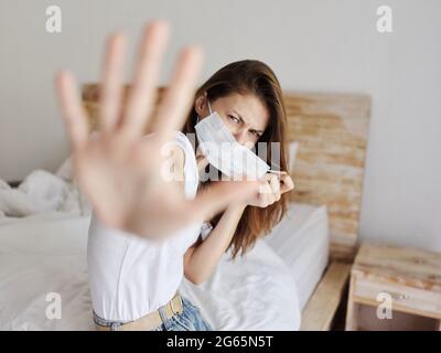 Reizbare Frau bedeckt sich mit den Händen von der Kamera und sitzt drinnen auf dem Bett Stockfoto