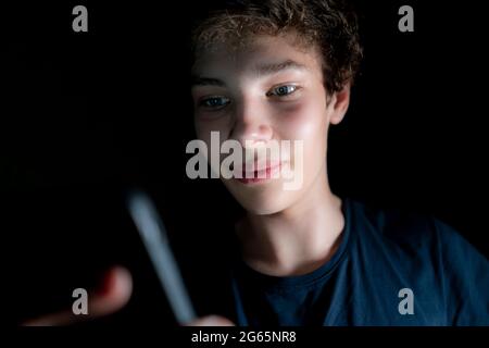 Ein junger attraktiver Mann nutzt in einem dunklen Raum spät in der Nacht das Handy Stockfoto